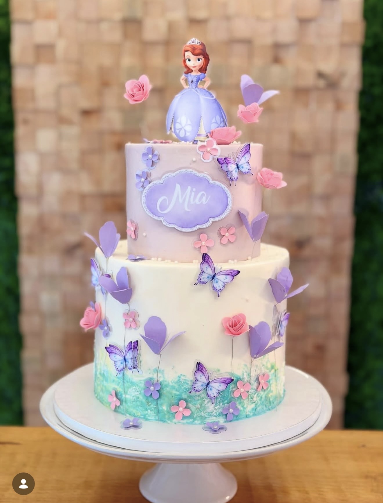 Princesa Sofia — Bolo em tons lilás e rosa com borboletas, flores e jardim pintado à mão na base.